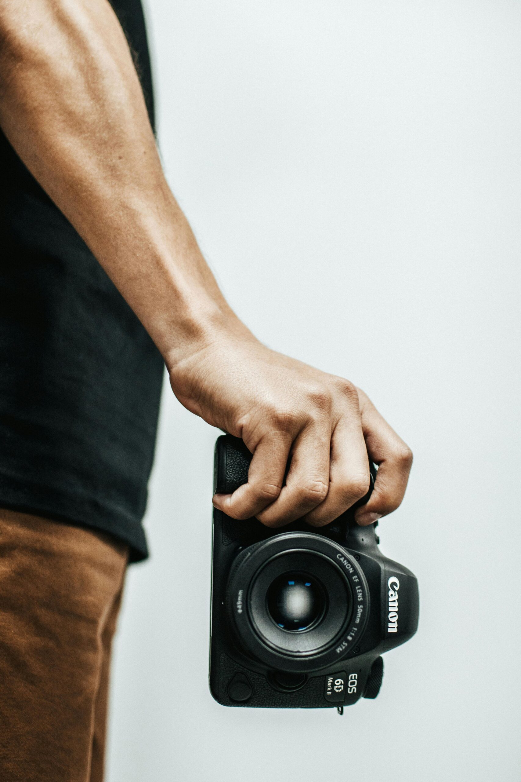 Aneesh Photography Close-up of a man holding a DSLR camera, focusing on the lens and grip.